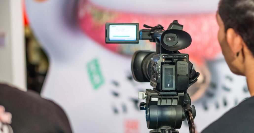 Someone who's standing behind a video camera that has a small screen on it. The camera is pointed at a very vibrant wall.