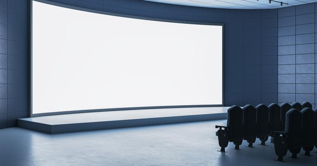 A giant, curved LED wall set up in front of a few rows of movie seats. There is a small stage in front of the screen.