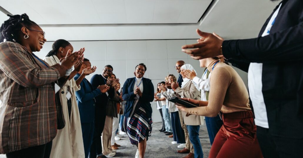 A woman walking through rows of people standing and clapping for her. Everyone looks very excited to be there.