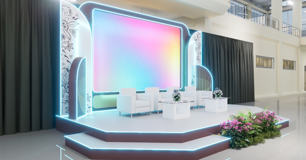 A white stage with blue trim along the stairs has screen with swirls of pastel colors is behind four cushioned white chairs.