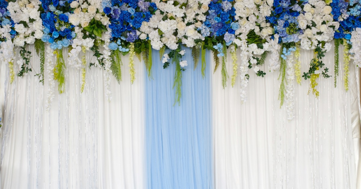 Blue and white flowers with green vines hang above white and pale blue draped fabric with small blue accents below.